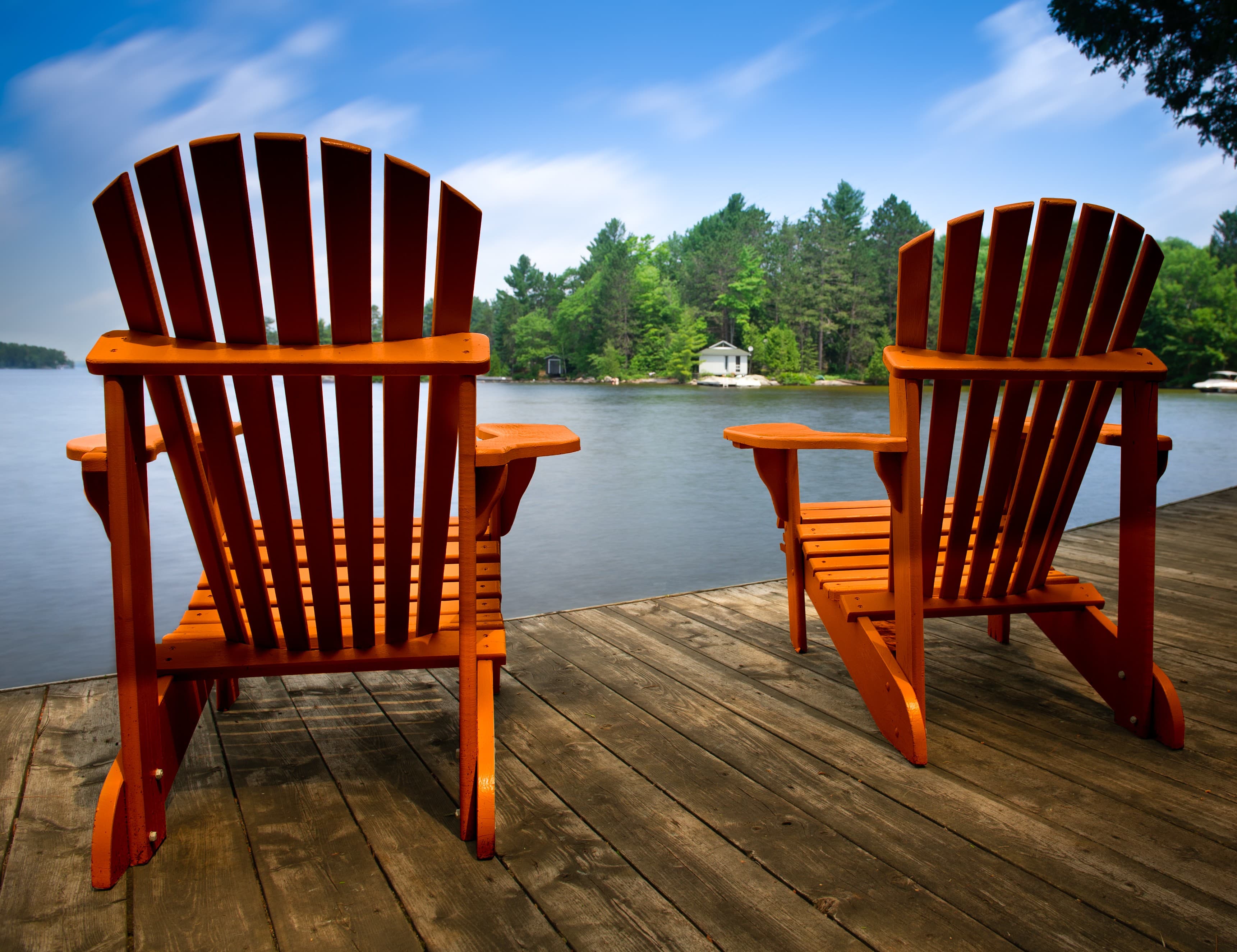 Two Adirondack chairs on a dock overlooking calm water